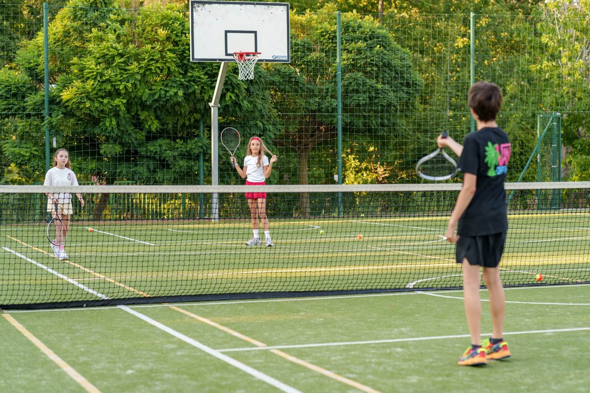 Children playing tennis together on an outdoor court at VIEC summer camp